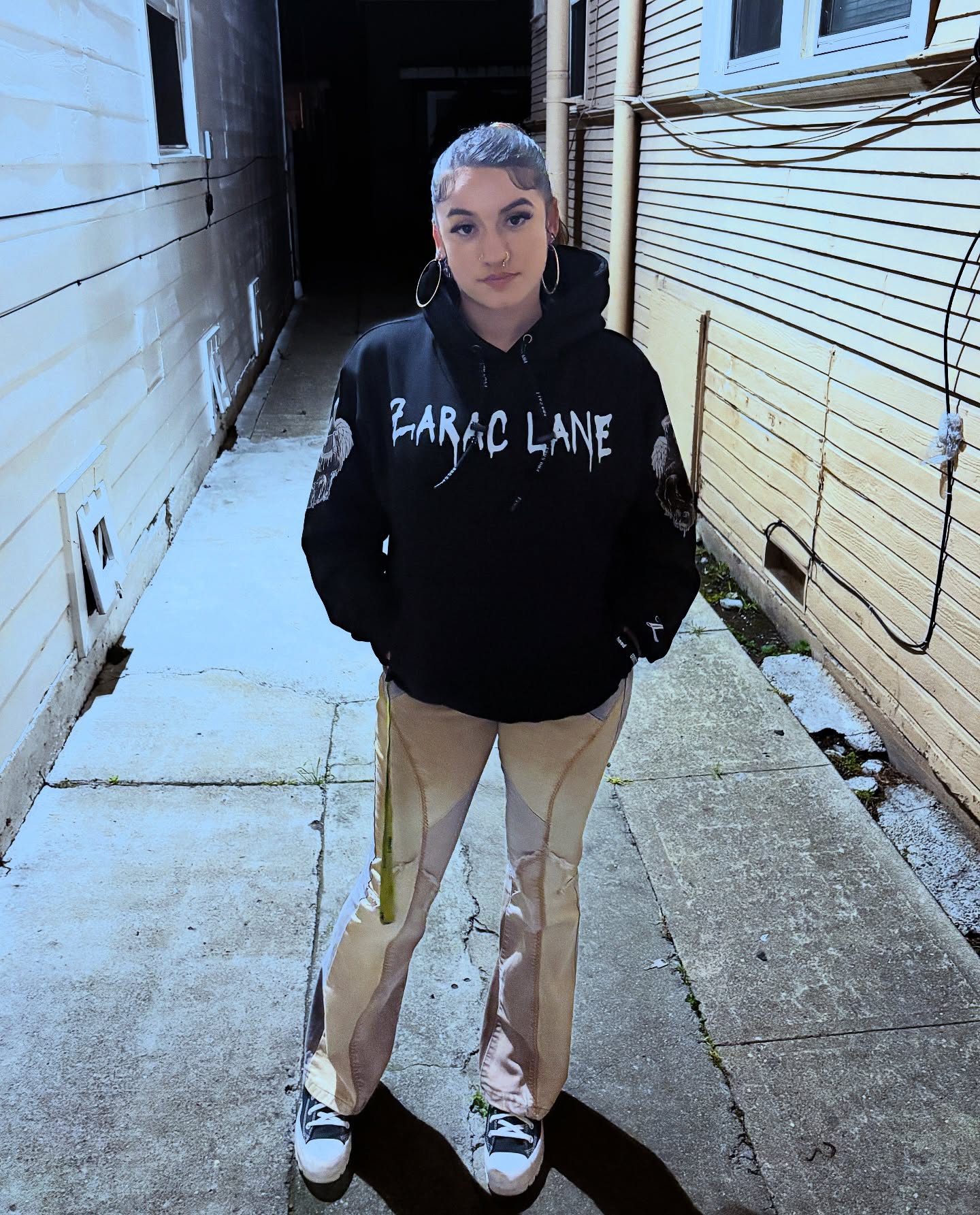 Person standing in an alleyway wearing a black ZARAC LANE hoodie